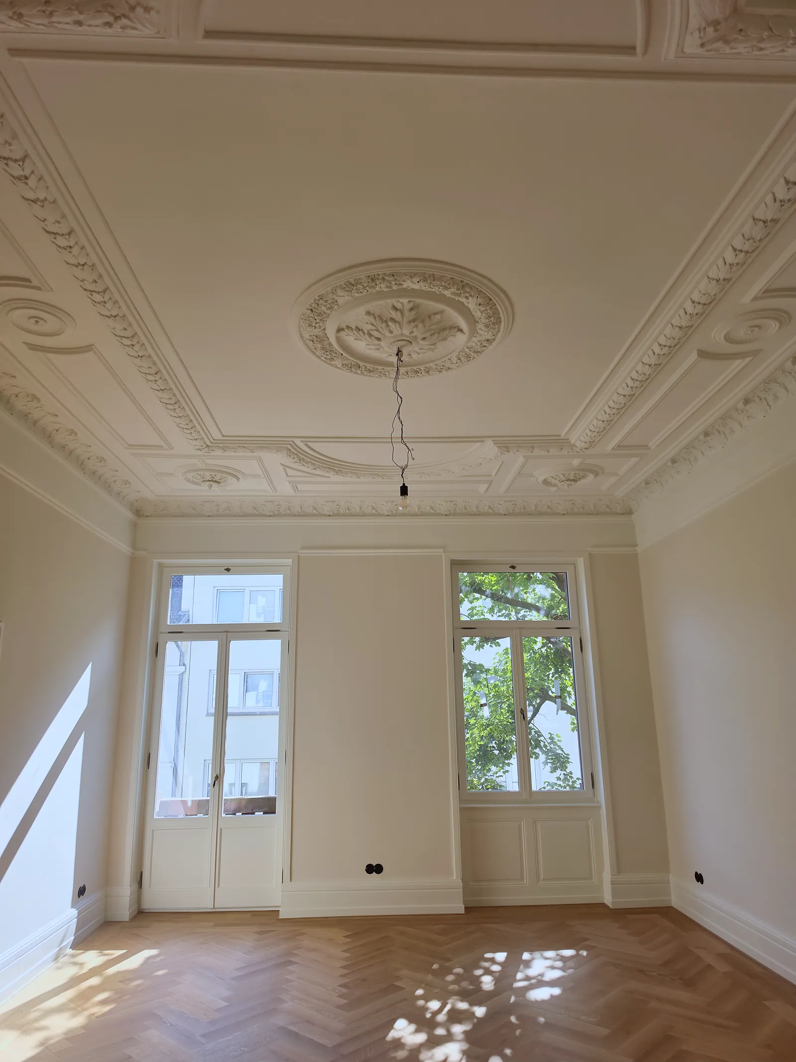 Salon ze sztukaterią na suficie, dwoma oknami i parkietem w jodełkę